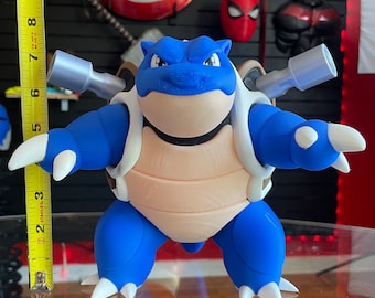 May include: A blue and beige plastic action figure of a turtle-like Pokemon character with silver cannons on its back. The figure is standing on a glass table.