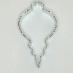 May include: A silver metal cookie cutter shaped like a Christmas ornament. The ornament has a rounded top and a pointed bottom.