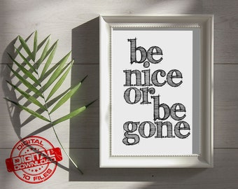 May include: A white framed print with the text "be nice or be gone" in black handwritten font. The print is on a white wooden surface with a green palm leaf.