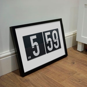 May include: A framed print of a vintage-style clock displaying 5:59 AM. The clock has black numbers on a white background.