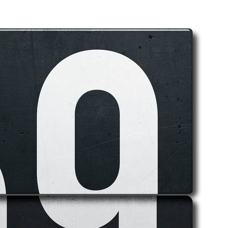 May include: A white number "0" on a black background. The number is made of a thick, bold font and is set against a textured, dark gray surface.