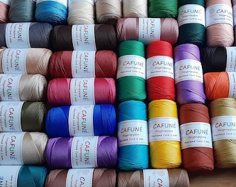 May include: A collection of numerous spools of 2 mm polypropylene macramé cord in a wide variety of solid colours. Each spool features a white paper label with the brand name CAFUNÉ, the material type, and the cord diameter printed in black text.