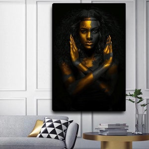 May include: A black and gold portrait of a woman with her arms crossed in front of her. Her face is painted half black and half gold.