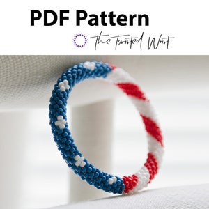 May include: A blue, white and red beaded bracelet with a pattern resembling the American flag. The bracelet is on a white surface.