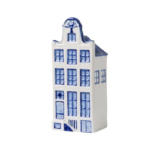 Op de afbeelding: Een wit keramisch huisbeeldje met blauwe accenten. Het miniatuurhuis heeft een traditioneel Nederlands ontwerp met meerdere ramen en een gedetailleerd dak. De ramen en architecturale details zijn geschilderd in een levendige blauwe kleur.