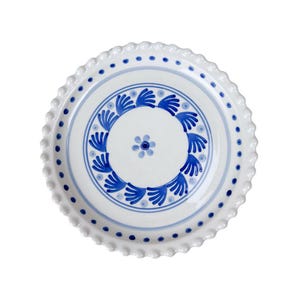 Op de afbeelding: Witte keramische plaat met een geschulpte rand en een blauw bloemmotief. De plaat heeft een centrale bloem en een rand van gestileerde blauwe bladeren en stippen. Een decoratief stuk om te serveren of tentoon te stellen.