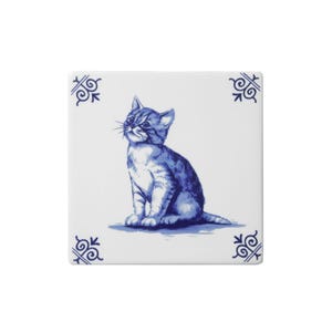 May include: Square ceramic tile with a blue and white illustration of a seated kitten. The design is reminiscent of Delftware, with decorative corner patterns. The kitten is detailed with shading, giving it a lifelike appearance.