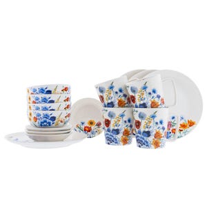 Op de afbeelding: Een wit servies met bloemmotief met blauwe, oranje en gele bloemen. De set bevat kopjes, kommen, borden en schotels. Het ontwerp wordt herhaald op elk stuk, waardoor een samenhangende en elegante uitstraling ontstaat.