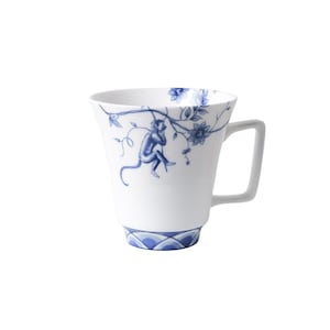 Può includere: Una tazza in ceramica bianca con un design floreale blu e bianco che presenta una scimmia appesa a un ramo. La tazza ha un bordo svasato e un manico.
