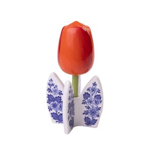 Könnte beinhalten: Eine orangefarbene Tulpe aus Holz mit roten Streifen steht in einer weißen Keramikvase mit einem blauen und weißen Blumenmuster.