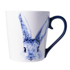 Op de afbeelding: Witte keramische mok met een blauwe aquarel illustratie van een konijn. De mok heeft een donkerblauwe handgreep. De oren van het konijn zijn lang en rechtopstaand, en de vacht is gedetailleerd met blauwe penseelstreken. Een charmante toevoeging aan elke keuken.
