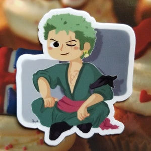 May include: A green and black cartoon sticker of a character with green hair, a black eye patch, and a pink sash. The character is sitting with one leg crossed over the other.