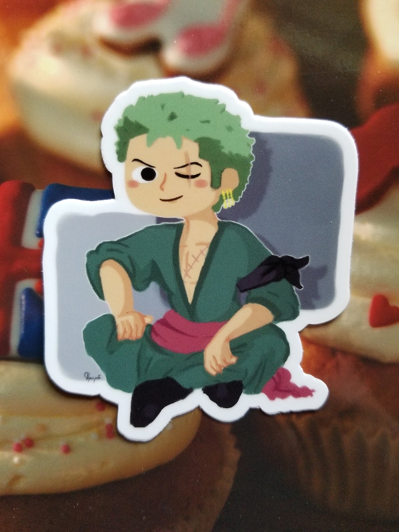 May include: A green and black cartoon sticker of a character with green hair, a black eye patch, and a pink sash. The character is sitting with one leg crossed over the other.