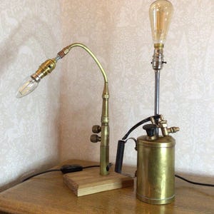 May include: A brass lamp with a vintage style light bulb and a brass and black sprayer base. The lamp is on a wooden base and has a cord and plug.