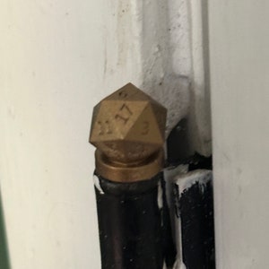 May include: A gold-colored metal door hinge with a decorative,  faceted,  d20 dice-shaped knob. The dice has the numbers 1, 2, 3, 4, 5, 6, 7, 8, 9, 10, 11, 12, 13, 14, 15, 16, 17, 18, 19, and 20 on its faces.