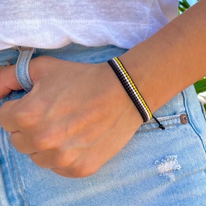 May include: A black, white and yellow beaded bracelet with a knotted closure.