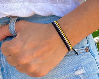 May include: A black, white and yellow beaded bracelet with a knotted closure.