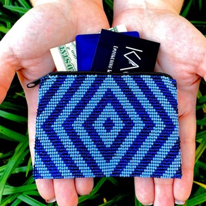 May include: A rectangular coin purse crafted from small beads in shades of dark blue and light blue, featuring a geometric diamond pattern. The purse has a black zipper closure and contains a US dollar bill, a blue card, and a black card with text.
