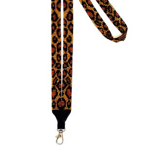 May include: A beaded lanyard with a leopard print design. The lanyard features a pattern of black, orange, and gold beads. It has a black fabric base and a silver-colored metal clasp.