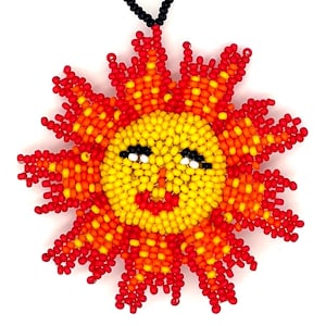 May include: A beaded sun ornament with a smiling face. The sun is made of yellow, orange, and red beads, with a black beaded loop for hanging. The sun's face has black eyes and a red smiling mouth.