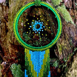 May include: A green, yellow, and blue beaded dreamcatcher with a circular frame and beaded fringe hanging from a tree trunk.