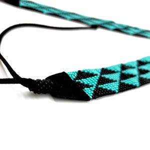 May include: A turquoise and black beaded necklace with a black leather cord. The necklace features a geometric pattern of triangles.