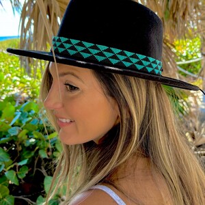 May include: A black fedora hat with a turquoise and black beaded band. The hat is worn by a person with long blonde hair.