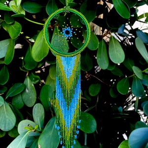 May include: Green, blue, and yellow beaded dreamcatcher with a fringe of beads. The dreamcatcher is hanging from a green cord.