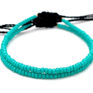 Puede incluir: Pulsera de cuentas turquesa con cierre ajustable negro. La pulsera está hecha de pequeñas cuentas redondas turquesas. El cierre ajustable es de hilo negro.