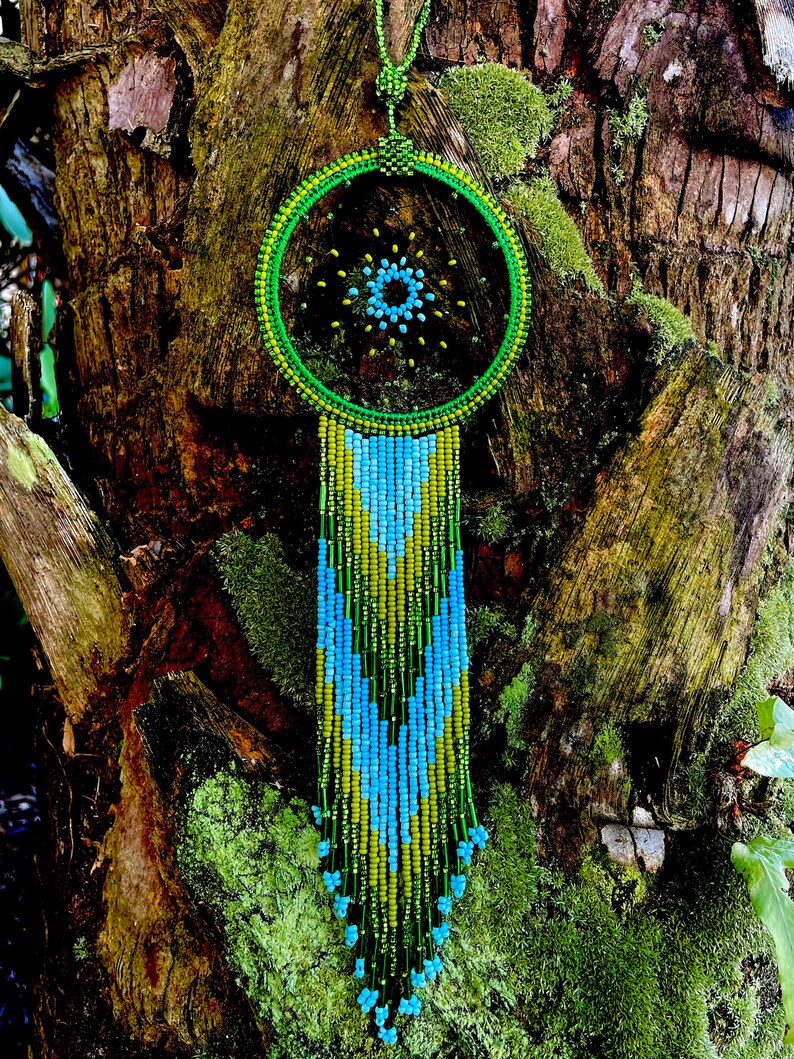 May include: A green and blue beaded dreamcatcher with a circular beaded design and a long beaded fringe hanging from the bottom.