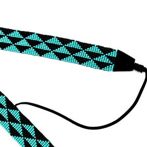 May include: A black and turquoise beaded necklace with a geometric pattern of triangles. The necklace has a black cord that can be adjusted to fit different neck sizes.