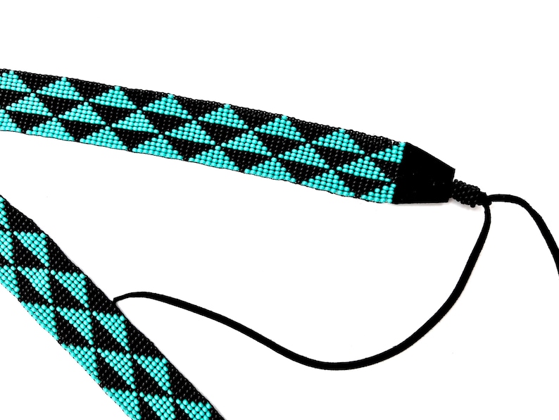 May include: A black and turquoise beaded necklace with a geometric pattern of triangles. The necklace has a black cord that can be adjusted to fit different neck sizes.