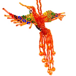 Könnte beinhalten: Ein Perlen-Kolibri-Anhänger mit einem langen, fließenden Schwanz. Der Kolibri besteht aus orangefarbenen, grünen, blauen und gelben Perlen. Der Schwanz besteht aus orangefarbenen Perlen.