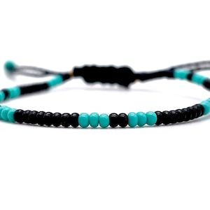 Op de afbeelding: Een turquoise en zwarte kralen armband met een zwarte koordsluiting.