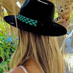 May include: A black fedora hat with a turquoise and black beaded band. The hat is worn by a person with long blonde hair.