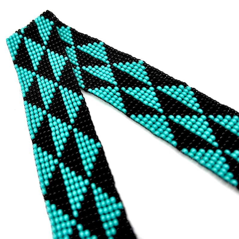 May include: A black and turquoise beaded strap with a chevron pattern. The strap is made of small beads woven together to create a geometric design.