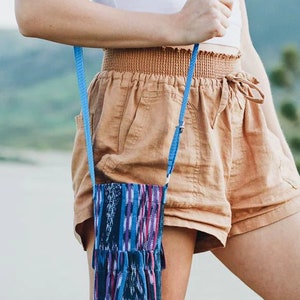May include: A woman wearing brown shorts and a white tank top carries a blue and black patterned fabric bag with a blue strap.
