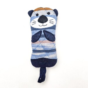 May include: A blue and brown striped plush toy shaped like an otter with a smiling face. The toy has a long tail and is made of soft fabric.