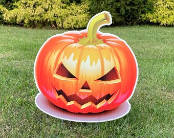 May include: A large orange pumpkin with a carved jack-o'-lantern face is displayed on a green lawn. The pumpkin has a wide, toothy grin and menacing eyes.