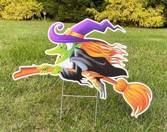 May include: A witch with a purple hat and orange broom flies through the air. The witch is green and has orange hair. The background is a green lawn with trees in the background.