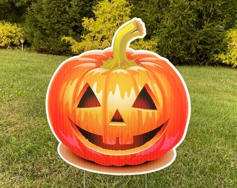 May include: A large orange and red jack-o'-lantern with a carved face is displayed on a lawn. The pumpkin is on a metal stake.