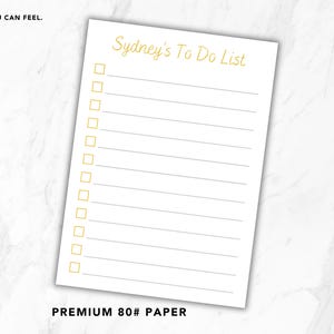 May include: A white to-do list notepad featuring the gold text Sydney's To Do List at the top, with twelve gold square checkboxes and horizontal lines. The paper is labeled as premium 80# paper, with the text Quality You Can Feel. Small Detail. Big Difference.