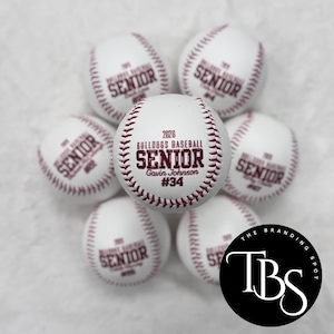 May include: White baseballs with maroon stitching and text. The central ball reads "2026 BULLDOGS BASEBALL SENIOR Gavin Johnson #34." Other balls display "SENIOR" and a number. A black circle with "TBS" is in the corner.