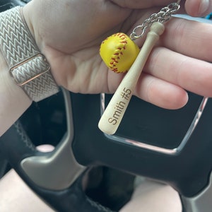 May include: A wooden baseball bat keychain with a yellow softball charm. The bat is engraved with "Smith #5".