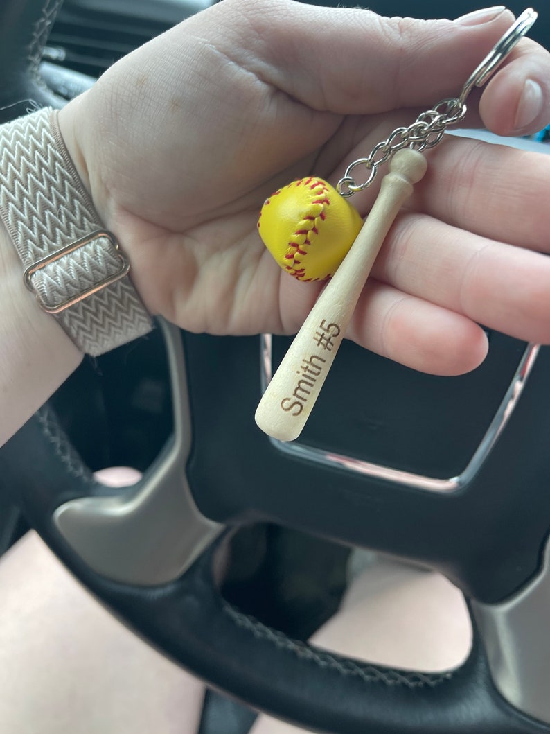May include: A wooden baseball bat keychain with a yellow softball charm. The bat is engraved with "Smith #5".