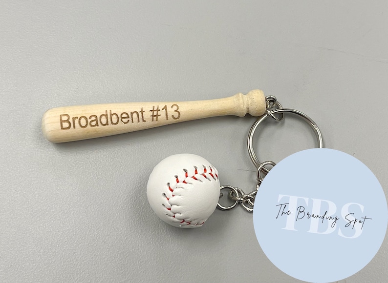 May include: A wooden baseball bat keychain with the name "Broadbent #13" engraved on it. The keychain also features a white baseball and a blue circle with the text "The Branding Spot" in white.