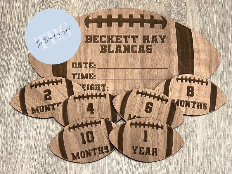 May include: A wooden football-shaped milestone sign with the name "BECKETT RAY BLANCAS" engraved at the top. Includes smaller footballs marked "2 MONTHS", "4", "6 MONTHS", "8 MONTHS", "10 MONTHS", and "1 YEAR".