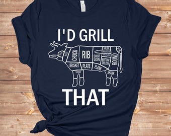 Può includere: Una maglietta blu navy con una grafica bianca di una mucca tagliata in diversi tagli di carne. Il testo "I'd Grill That" è stampato sotto la mucca.