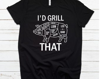Può includere: Maglietta nera con una grafica bianca di un maiale con diversi tagli di carne etichettati. Il testo "I'd grill that" è sotto il maiale.