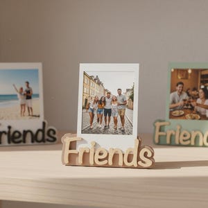 Könnte beinhalten: Drei Fotorahmen mit dem Wort "Friends" an der Basis. Jeder Rahmen enthält ein anderes Foto. Die Rahmen sind in Schwarz, Naturholz und Hellgrün gehalten. Die Fotos zeigen Menschen.
